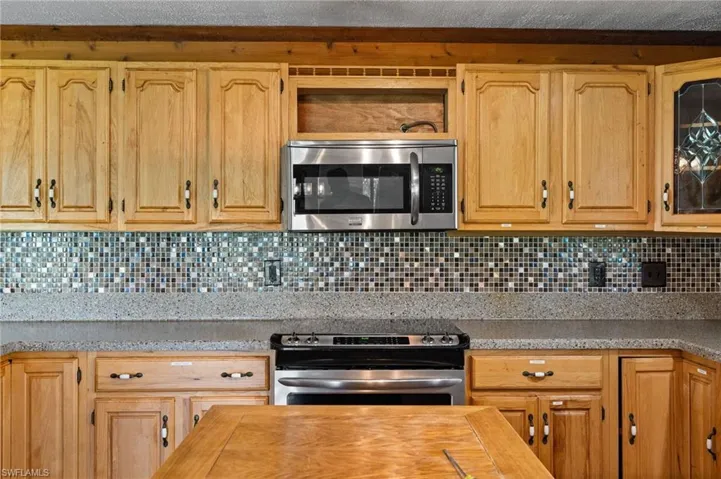 Kitchen featuring natural wood cabinetry, mosaic tile backsplash, solid surface countertops, stainless steel microwave, and range