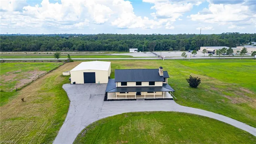 Expansive property featuring a two-story residence with a covered porch and dark metal roof, a large detached industrial-style building with a roll-up door, and a paved driveway
