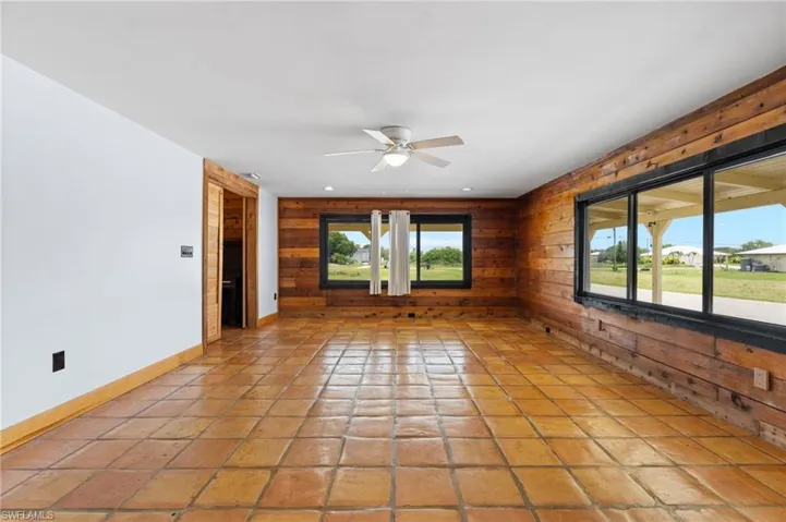 Spacious room featuring terracotta tile flooring and a wood-paneled accent wall