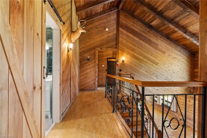 Vaulted wood-paneled ceilings with exposed beams, wood-finish flooring, and a decorative wrought iron and wood banister