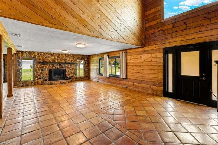 Expansive living space featuring extensive wood paneling, a stone-clad fireplace, and terracotta tile flooring
