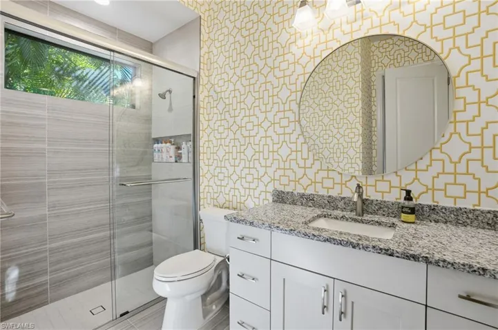 Bathroom featuring wallpapered walls, vanity, and a stall shower