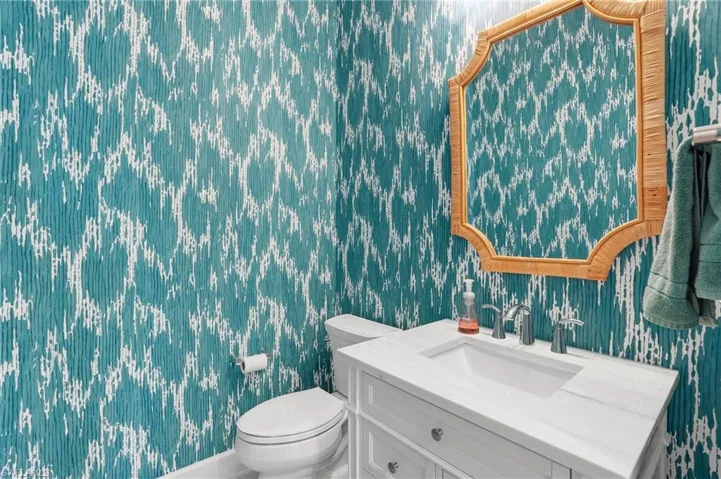 Half bath featuring wallpapered walls and vanity