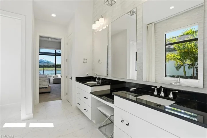 Full bathroom featuring double vanity, light marble finish floors, a water view, and recessed lighting
