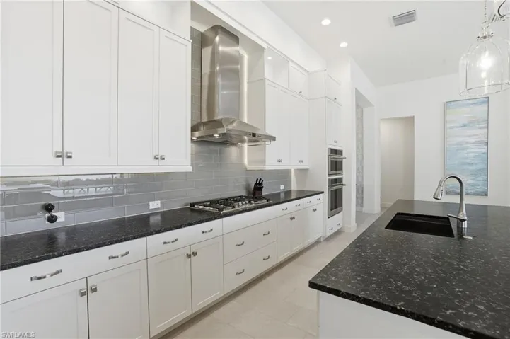 Kitchen with white cabinetry, wall chimney range hood, dark stone counters, tasteful backsplash, and recessed lighting