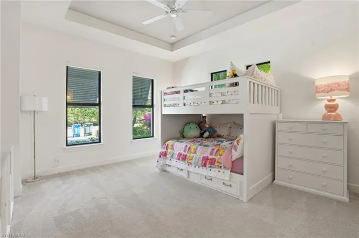 Bedroom with light carpet, ceiling fan, and a raised ceiling
