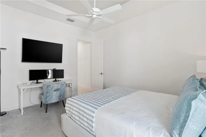 Bedroom with light carpet, ceiling fan, and a desk