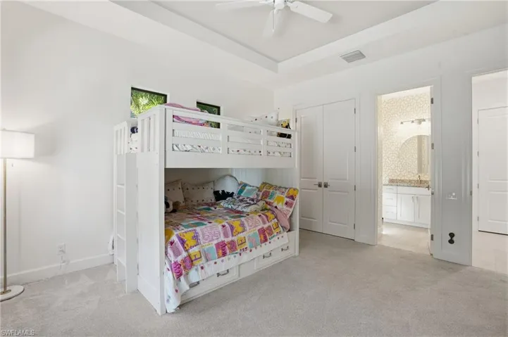 Bedroom featuring light carpet, a closet, ceiling fan, a raised ceiling, and ensuite bath