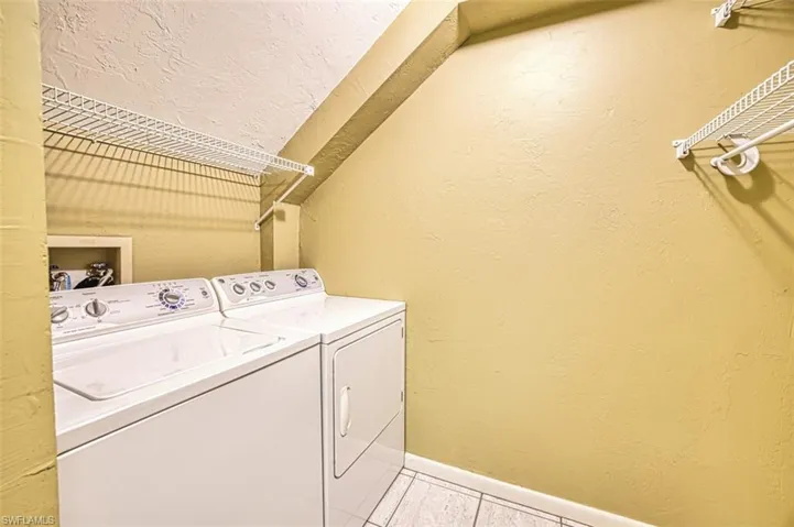Washroom featuring a textured wall, light tile patterned floors, washing machine and dryer, and a textured ceiling