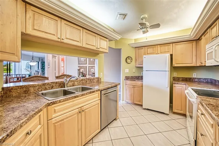 Kitchen with light brown cabinets, white appliances, light tile patterned floors, and ceiling fan