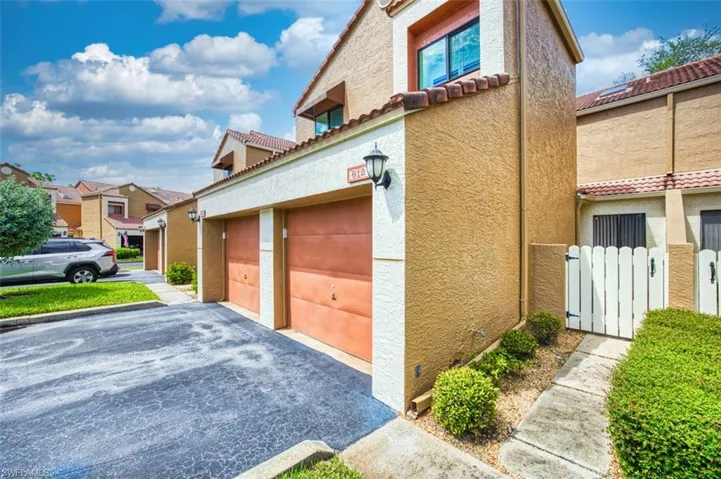 View of side of home featuring a garage, stucco siding, a tile roof, and driveway
