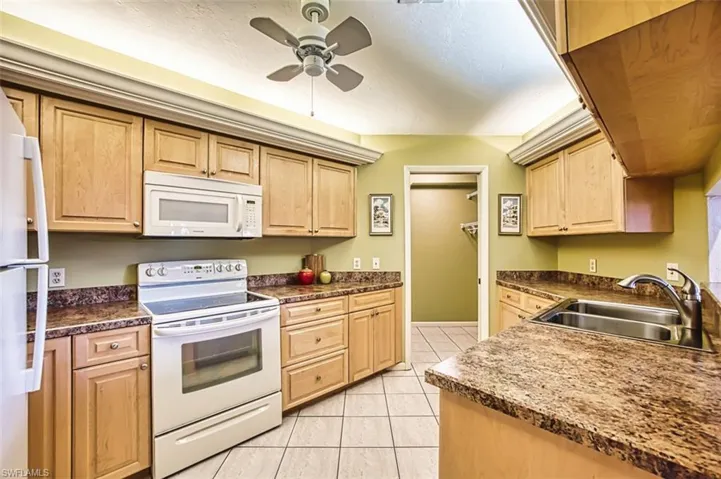 Kitchen featuring white appliances, light brown cabinets, light tile patterned floors, and a ceiling fan