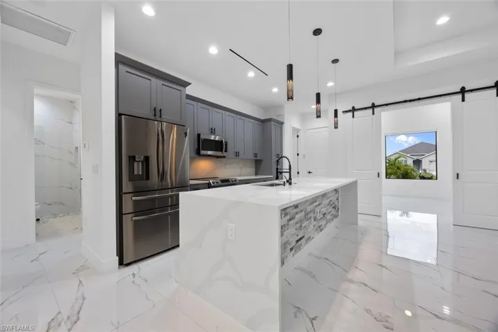 Kitchen with appliances with stainless steel finishes, decorative light fixtures, light stone counters, and a barn door