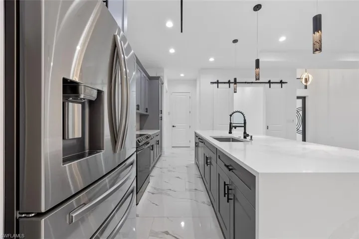 Kitchen featuring decorative light fixtures, a barn door, a sink, stainless steel fridge, and a large island with sink