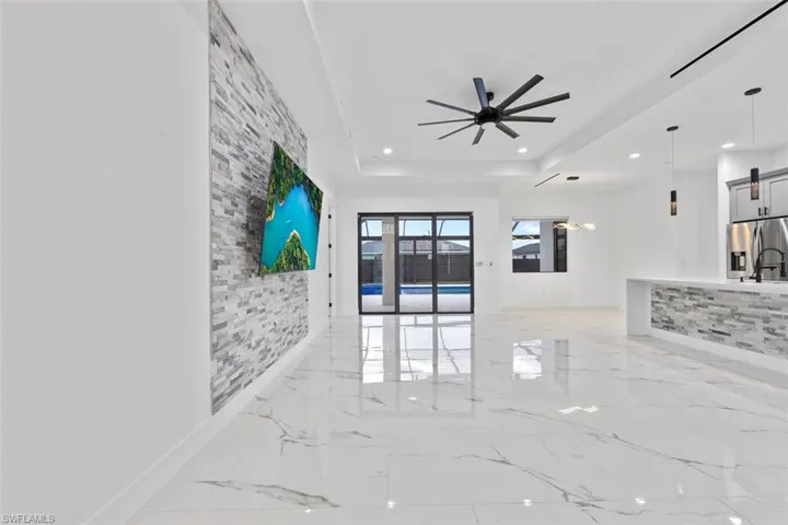 Living area with ceiling fan, marble finish floor, a raised ceiling, and recessed lighting