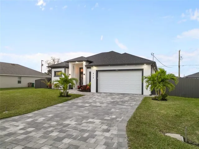 Prairie-style home featuring decorative driveway, stucco siding, an attached garage, fence, and a front lawn