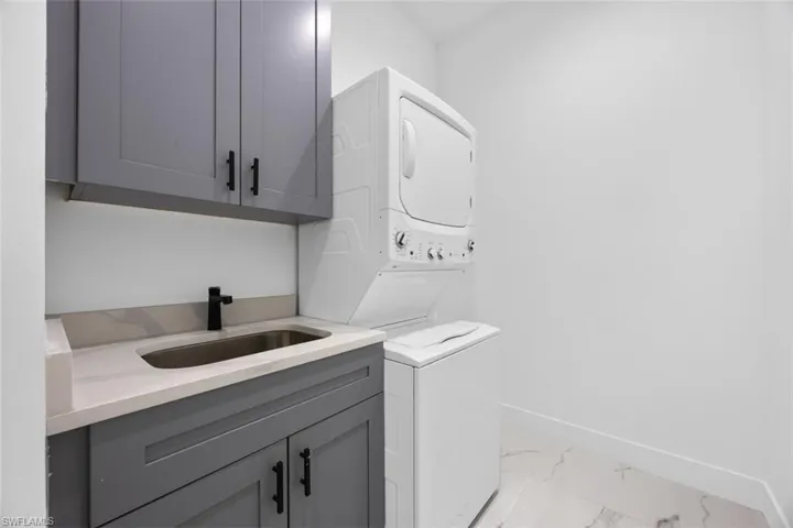 Laundry area with a sink, baseboards, marble finish floor, cabinet space, and stacked washer and clothes dryer