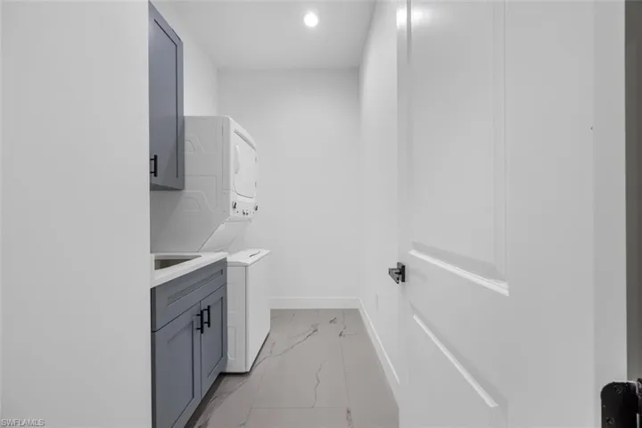 Clothes washing area featuring marble finish floor, recessed lighting, cabinet space, stacked washer / dryer, and baseboards