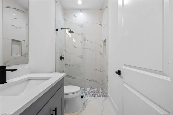 Full bathroom with a marble finish shower, toilet, marble finish floor, vanity, and recessed lighting