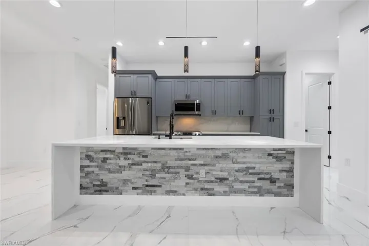Kitchen with hanging light fixtures, appliances with stainless steel finishes, light countertops, and gray cabinetry