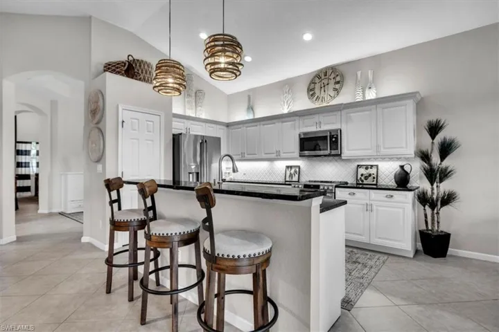 Kitchen featuring vaulted ceilings, white cabinetry, stainless steel appliances, black countertops, and a subway tile backsplash