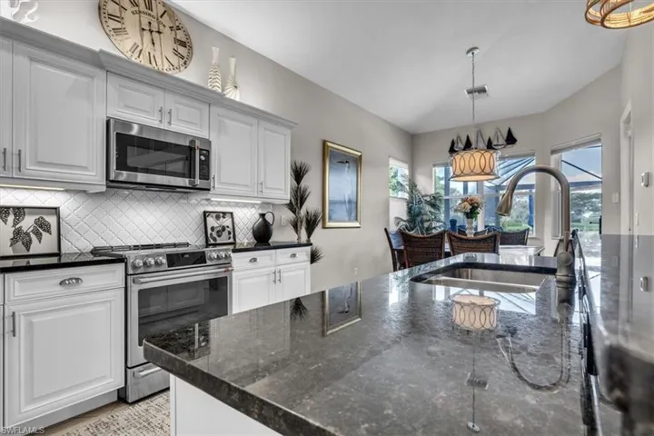 Kitchen featuring white shaker-style cabinetry, black stone countertops, stainless steel appliances, a tile backsplash, and an undermount sink with a gooseneck faucet