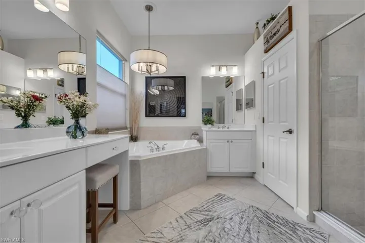 Dual vanity with integrated dressing table, soaking tub, glass-enclosed shower, and tiled flooring