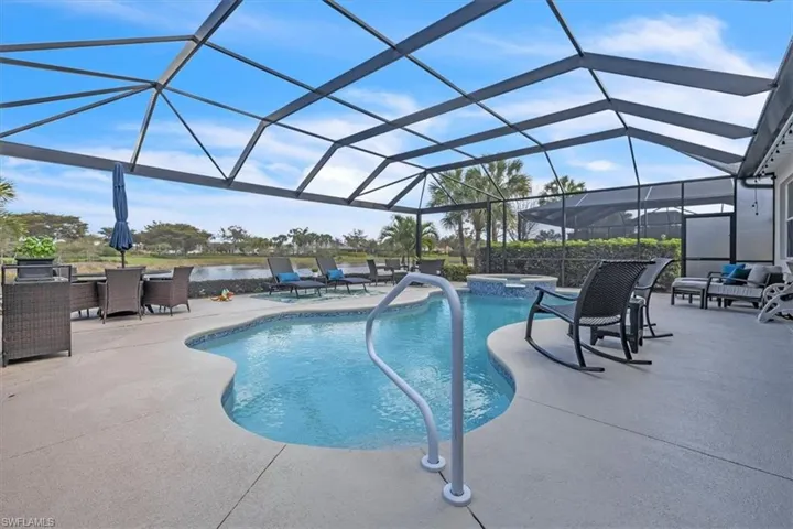Screened outdoor living area featuring a freeform pool, integrated spa, and ample paved decking
