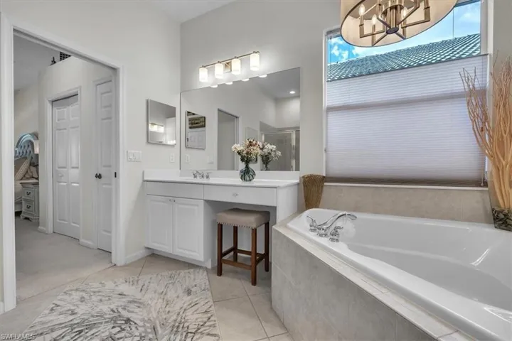 Built-in soaking tub with tile surround, dual vanity with undermount sinks, and an expansive mirror