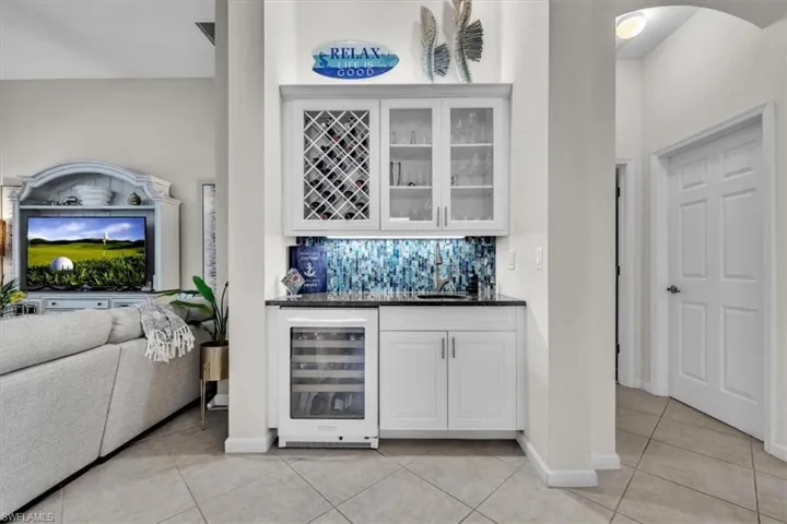 Custom built-in wet bar featuring white cabinetry, a glass-front wine rack, a compact beverage refrigerator, and a dark countertop