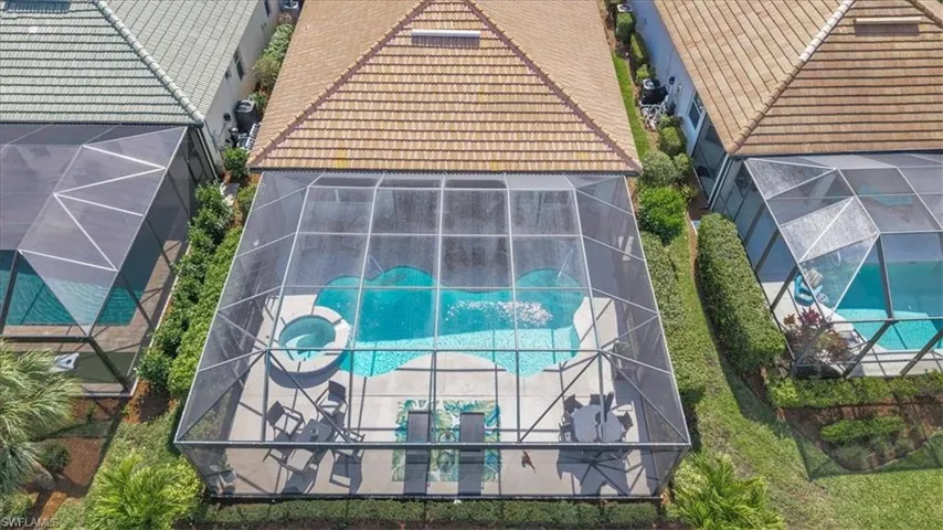 Screened-in outdoor living space featuring a freeform pool, integrated spa, and paved pool deck