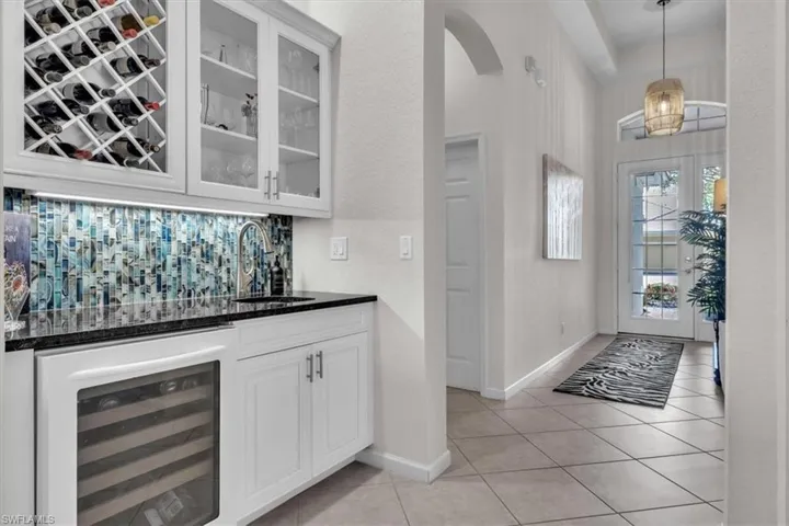 Built-in wet bar with wine rack, glass-front cabinetry, mosaic tile backsplash, and beverage refrigerator