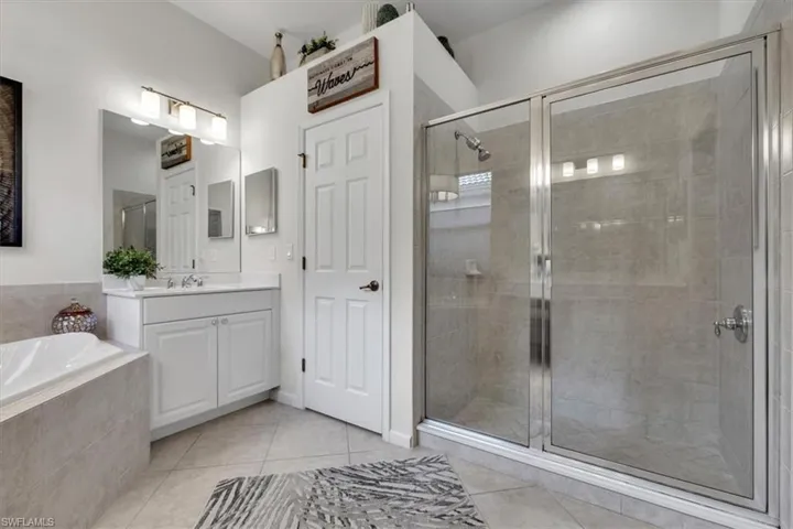 Glass-enclosed shower, white vanity with integrated sink, rectangular mirror, recessed lighting, and tile flooring