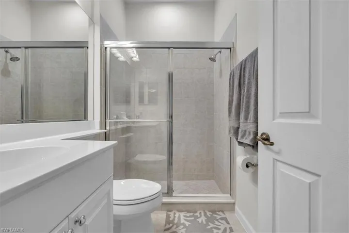 White vanity with integrated sink, chrome hardware, frameless mirror, glass-enclosed shower, and tile flooring