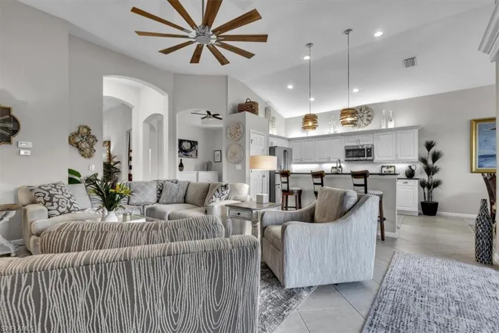 Vaulted ceiling with an overhead fan, arched doorways, tile flooring, kitchen island with seating, and stainless steel appliances