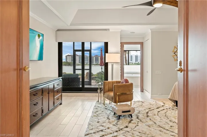 Primary bedroom with direct lanai access featuring light wood-type tile flooring, ceiling fan, and ornamental molding. En suite bathroom, large walk-in closet.