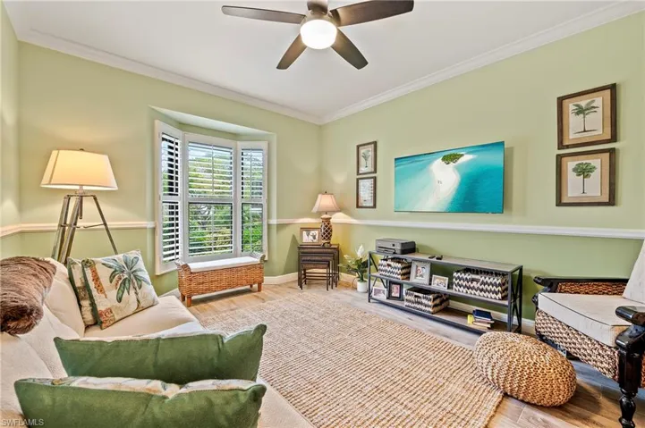 Guest bedroom/sitting room featuring ceiling fan, wood-style tile floors, and ornamental molding, built-in desk, and closet.