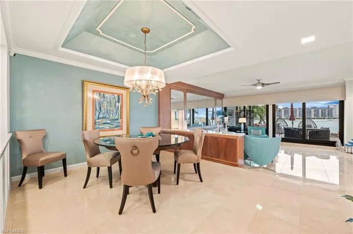 Dining area with tray ceiling, crown molding, chandelier. Step down to living room area with custom mirror, built-in shelving, screened-in lanai.