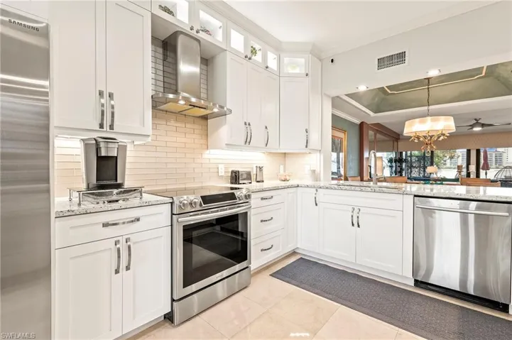 Kitchen featuring white cabinetry, appliances with stainless steel finishes, glass subway-tiled backsplash, wall chimney exhaust hood, and sink.