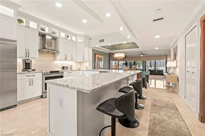 Kitchen with stainless steel appliances, ceiling fan, white cabinets, and wall chimney range hood. Breakfast bar, water views.