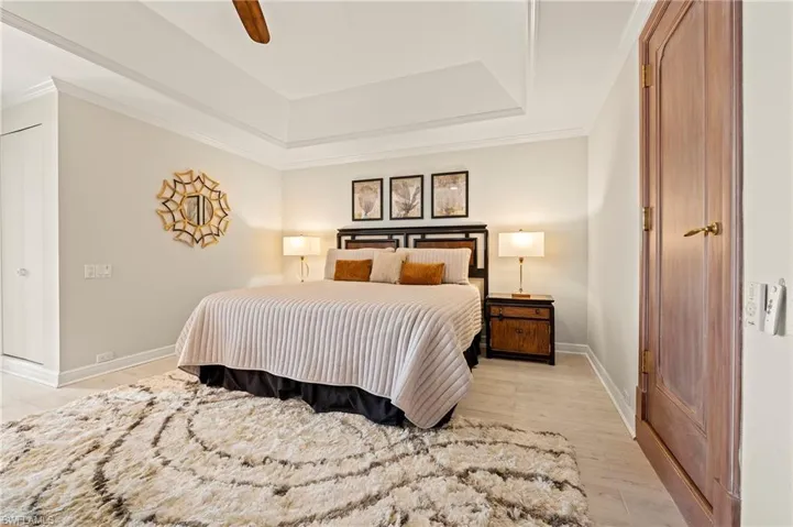 Primary Bedroom with light wood-type tile flooring, ceiling fan, crown molding, and a tray ceiling.