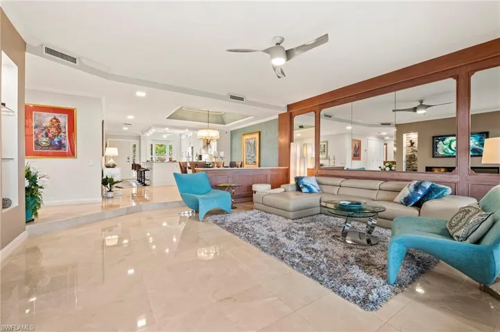 Living room with a raised ceiling, crown molding, and ceiling fan with notable chandelier