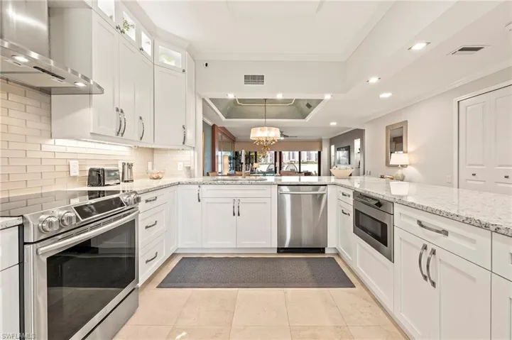 Kitchen with white cabinetry, stainless steel appliances, a raised ceiling, tasteful backsplash, and wall chimney exhaust hood.