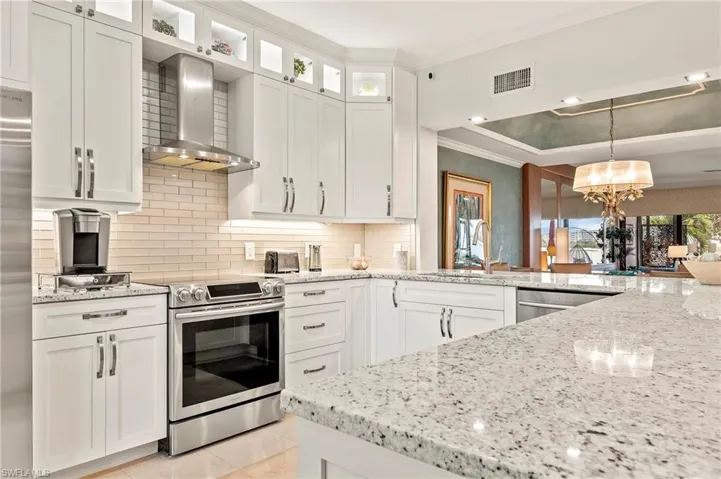 Kitchen featuring white cabinets, decorative light fixtures, wall chimney range hood, stainless steel appliances, and sink.