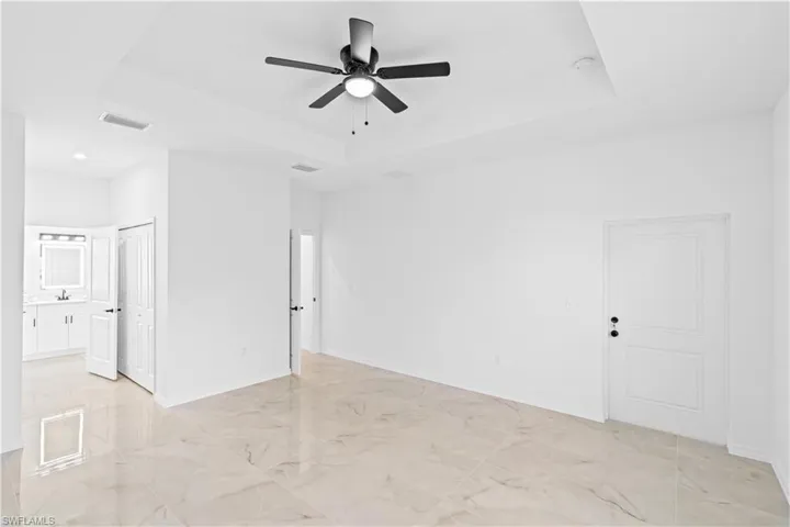 Empty room with a tray ceiling, a ceiling fan, and light marble finish flooring