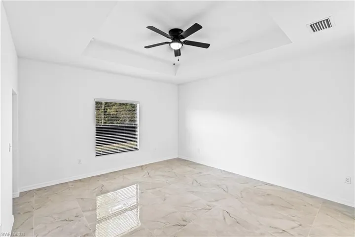 Unfurnished room featuring a tray ceiling, light marble finish flooring, and a ceiling fan