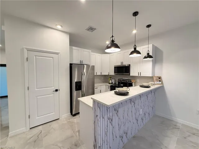 Kitchen featuring light marble finish floors, appliances with stainless steel finishes, a peninsula, white cabinetry, and hanging light fixtures