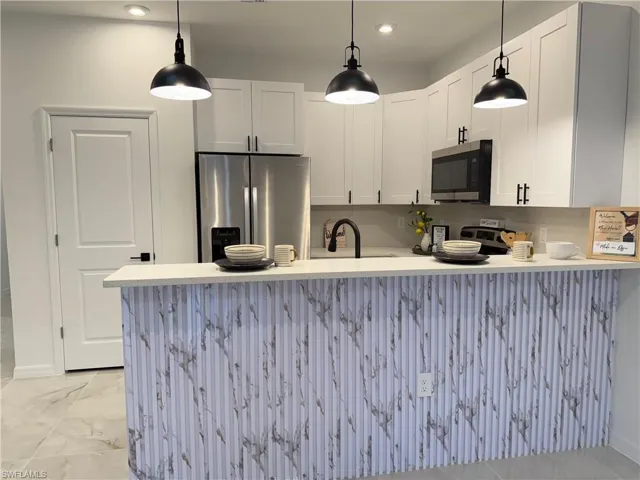 Kitchen with appliances with stainless steel finishes, light countertops, a peninsula, white cabinets, and pendant lighting
