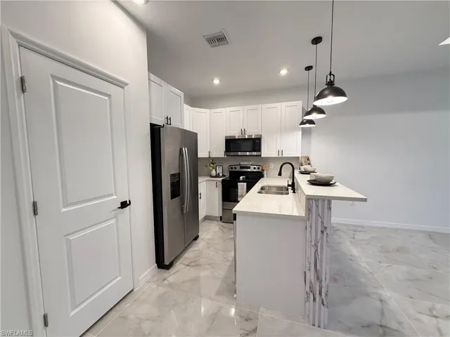 Kitchen featuring light marble finish flooring, appliances with stainless steel finishes, a kitchen bar, white cabinets, and a peninsula