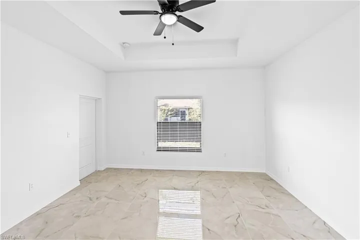 Empty room with a tray ceiling, light marble finish flooring, and a ceiling fan
